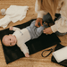 A baby boy is laying down on a black change mat waiting for his nappy to be changed.