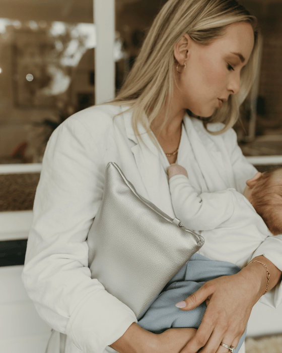 A mum wearing a stylish white blazer and metallic silver clutch rocks her baby to sleep.